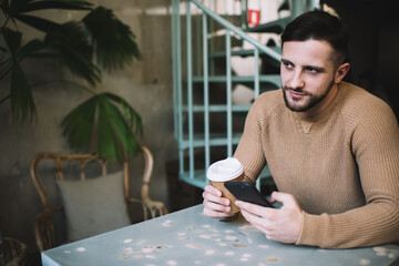 Young male sitting at table with coffee and smartphone