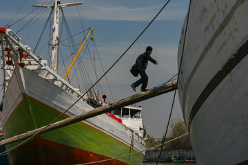 a man ascends a wooden ship on a wooden beam in front of a wooden ship in white, green and red