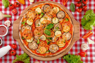 Vegetarian tasty pizza with vegetables, zucchini, eggplant, mushrooms, slices of tomato, fresh basil and tomatoes sauce on a wooden board, rustic village background, top view. 