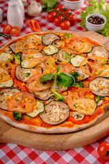Vegetarian tasty pizza with vegetables, zucchini, eggplant, mushrooms, slices of tomato, fresh basil and tomatoes sauce, rustic village background, top view. European and American cuisine.