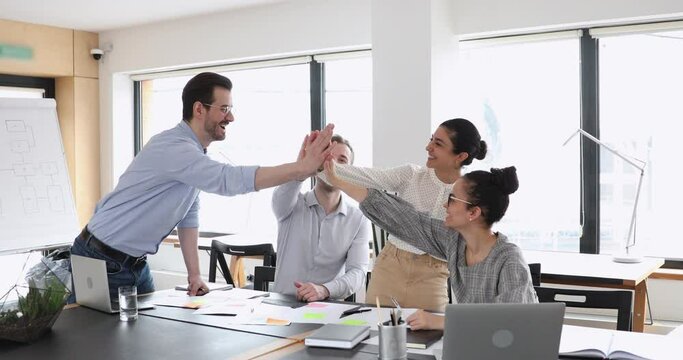 Motivated multicultural happy business people give high five at office meeting. African, caucasian and indian employees team celebrate leadership, professional success, good teamwork strategy concept.