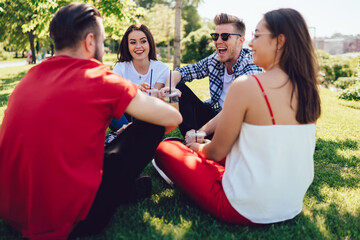 Smiling male and female colleagues with non alcohol cocktails for refreshing during hot summer day enjoying gather picnic meeting in park, joyful hipster guys rejoicing while discussing funny stories
