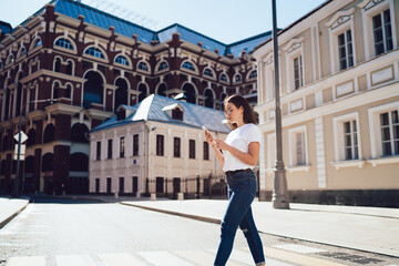 Fototapeta na wymiar Caucasian female user walking in touristic city connecting to roaming internet for tracking gps during sightseeing, millennial hipster girl exploring town searching online guide on smartphone gadget