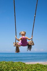 Happy girl have fun swinging high in mid air. Flying up upside down on rope swing on sea beach. Travel adventure on paradise tropical island. Family lifestyle, activity on summer vacation with kids