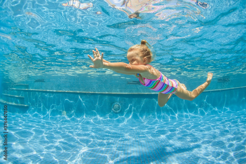 Wall mural Funny portrait of child learning swimming, dive in blue pool with fun - jumping deep down underwater with splashes. Healthy family lifestyle, kids water sports activity, swimming lesson with parents.