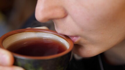 Woman blows on black tea and dinks it from ceramic tea cup. Art of tea concept