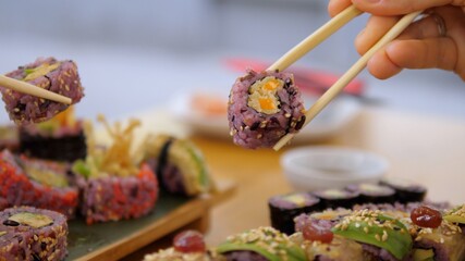 Dinner at Japanese restaurant. Side view of two hands holding colorful sushi rolls with chopsticks. Artisan oriental cuisine concept