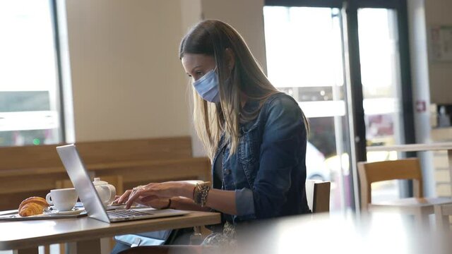 Young woman sitting at coffee shop and working on laptop 