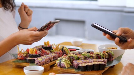 Two people taking pictures of their colorful vegan sushi sets with smartphones during lunch. Healthy vegan lifestyle concept