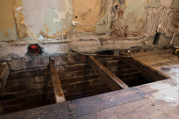 Hole in floorboards during home renovation showing into house foundations with rotting damaged joists and bare plaster walls