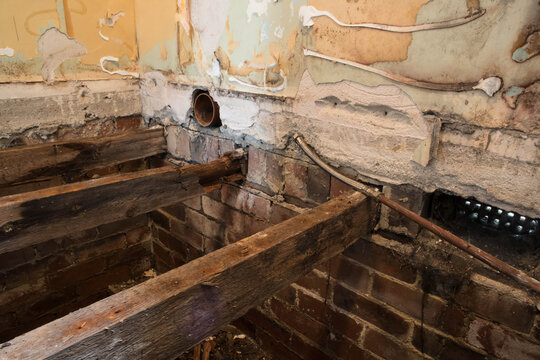 Hole in floorboards during home renovation showing into house foundations with rotting damaged joists and bare plaster walls