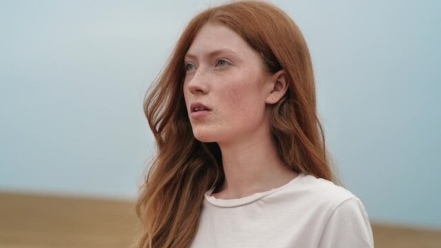 Beautiful Woman Ginger opening her Eyes while looking at Nature, having long nice Eyelashes. Attractive girl with nice Freckles on her Beautiful Face. Red-haired woman with walking on gold Field.