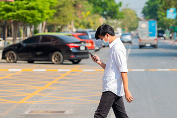 Young asian man in protective masks and looking at screen of smartphone while walking in the city street. Copy space