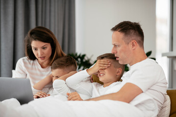 Beautiful parents with kids enjoying at home. Young family watching movie on lap top..