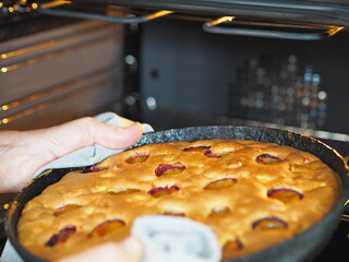 An elderly woman is hands take out a pan of ready made apple and plum pie from the kitchen oven. Homemade baking. Woman is hobby.