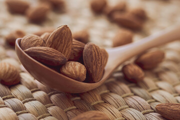 Closeup of brown fresh almonds seed in wooden spoon on wooden table.