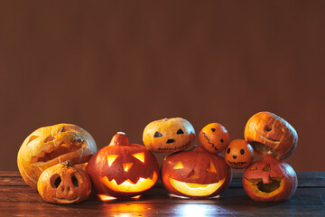 Horizontal studio shot of Halloween still life composition made of carved pumpkins and tangerines on brown background, copy space