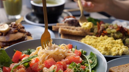 Close up of hand using forks for lunch of scramble and pasta served in blue plates. 
