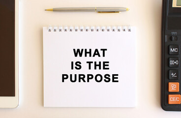 Notepad with text WHAT IS THE PURPOSE on a white background, near calculator, tablet and pen. Business concept.