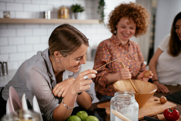 Girlfriends having fun in kitchen. Young women preparing delicious food at home.