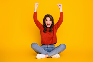 Obraz premium Full size photo of excited energetic girl sit floor legs crossed celebrate lottery win raise fists scream wear jeans jumper isolated bright shine color background