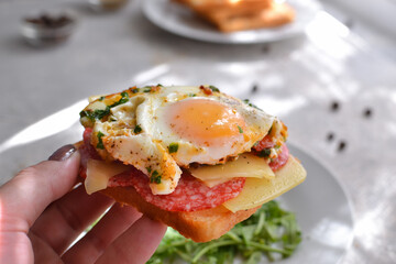Tasty breakfast. Toast with egg, cheese and sausage. The girl holds a toast, a sandwich in her hand. Closeup.