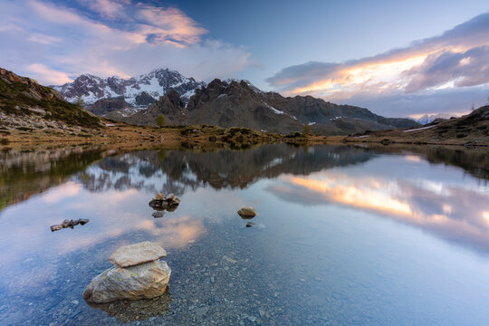Sunrise lit the rocky peak of Monte Disgrazia mirrored in the clear water of lake Zana, Valmalenco, Valtellina, Lombardy