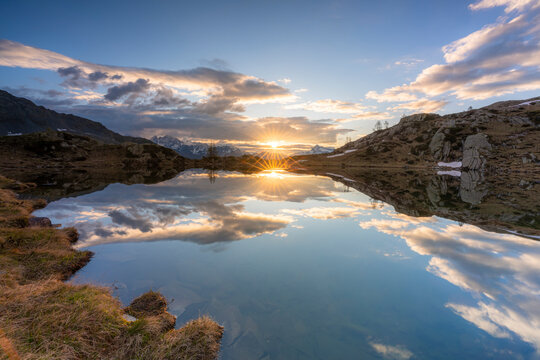 Sunburst over the clear waters of lake Zana during sunrise, Valmalenco, Sondrio province, Valtellina, Lombardy