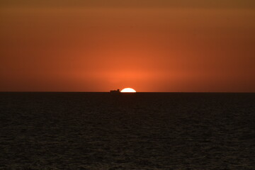 Naklejka na ściany i meble sunset on the sea, with a large cargo ship next to it