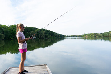 Cute woman is fishing with rod on the summer lake. Woman fishes on the river