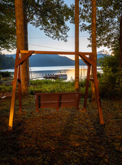Fototapeta premium A wooden swing at dusk overlooking a beautiful lake and a dock