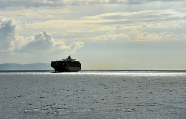 Fully loaded large container ship sailing near African coast on a cloudy day. 