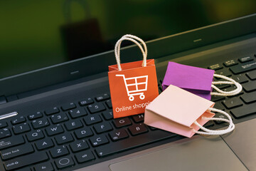 Small and colorful paper shopping bags on a laptop keyboard. Ideas about online shopping or shopping at home or office which customers can purchase items or services or goods remotely.