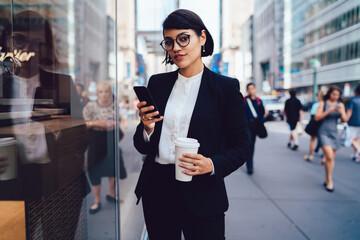 Charismatic businesswoman with smartphone and takeaway coffee