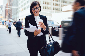 Smiling female executive with paper cup and documents on street