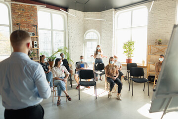 Male speaker giving presentation in hall at university workshop. Audience or conference hall. Young students, participants in audience wearing face mask. Scientific conference event, training
