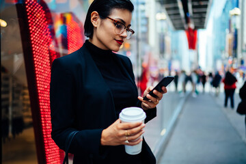 Elegant young lady messaging on street having coffee