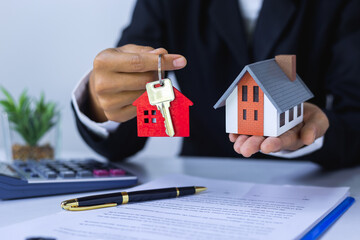 Gray roof houses and keys are in the hands of a businessman or an agent and for signing contracts,...