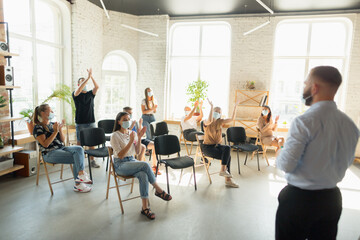 Male speaker giving presentation in hall at university workshop. Audience or conference hall. Young students, participants in audience wearing face mask. Scientific conference event, training
