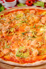 Rustic pizza macro with atlantic salmon, cheese, tomato, leek and tomatoes sauce in italian restaurant background, top view. Classic Italy food. Pizza from wooden oven. Close up