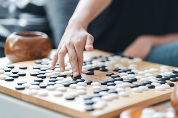 hand putting baduk black stone on wooden grid board - an ancient game also known as baduk in Korean, weiqi in Chinese and Igo in Japanese - obrazy, fototapety, plakaty