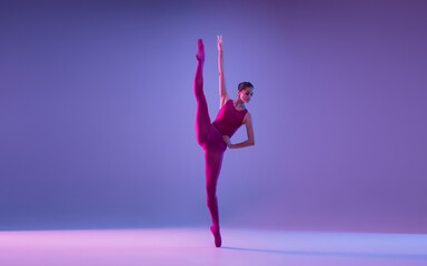 Direction. Young and graceful ballet dancer isolated on purple studio background in neon light....