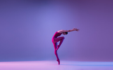 Direction. Young and graceful ballet dancer isolated on purple studio background in neon light. Art, motion, action, flexibility, inspiration concept. Flexible caucasian ballet dancer, weightless