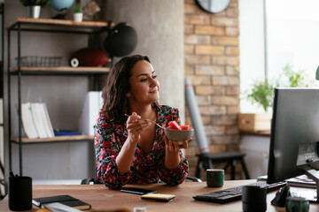 Businesswoman in office having healthy snack. Young businesswoman eating fruit while working.