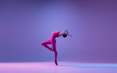 Fototapeta na wymiar Freedom. Young and graceful ballet dancer isolated on purple studio background in neon light. Art, motion, action, flexibility, inspiration concept. Flexible caucasian ballet dancer, weightless jumps.