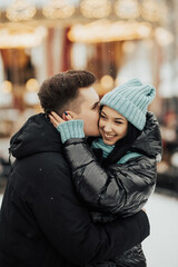 Happy man kissing and embracing smiling woman in winter in city. Love, winter holidays and people concept.