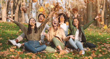 Happy students playing with golden leaves in park