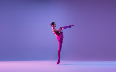 Tender. Young and graceful ballet dancer isolated on purple studio background in neon light. Art, motion, action, flexibility, inspiration concept. Flexible caucasian ballet dancer, weightless jumps.