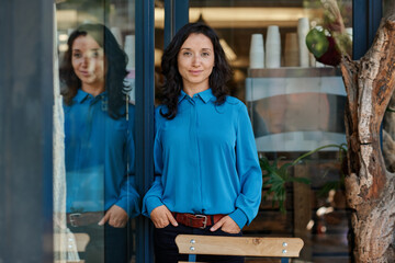 Smiling Asian female entrepreneur standing by the shop door