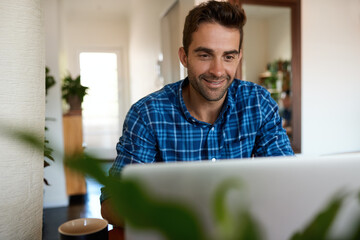 Smiling man using a laptop to work remotely from home